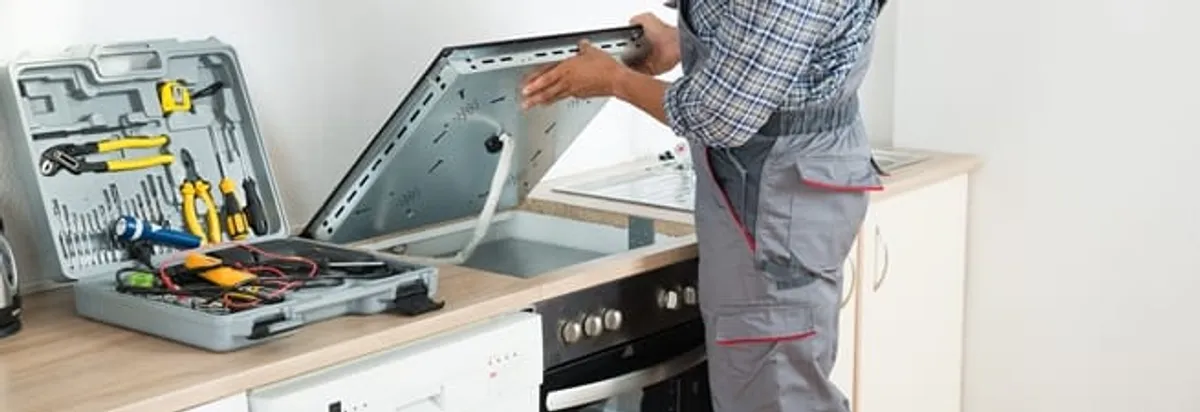 Cooktop repair technician lifting a built-in stovetop for service in Toledo, OH