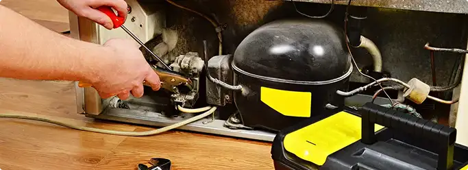 Refrigerator repair technician fixing the compressor and wiring in Toledo, OH